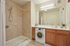 Modern bathroom featuring a stylish walk-in shower, convenient in-unit washer, and elegant vanity with warm wood cabinetry.