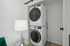 Contemporary laundry area with sleek stacked washer and dryer, complemented by a chic silver lamp and stylish decor.