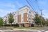 Modern apartment building exterior with elegant brick fa&ccedil;ade, lush landscaping, and a clear blue sky backdrop.