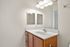 Sleek modern bathroom featuring a pristine white countertop, elegant wooden cabinetry, and bright overhead lighting.
