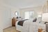 Bright and inviting bedroom with a cozy bed, elegant wooden dresser, and natural light streaming through large windows.