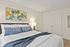 Charming bedroom with elegant decor, featuring a cozy bed with plush pillows, warm lighting, and vibrant abstract art above the headboard.