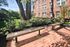 Charming outdoor patio area with elegant benches, surrounded by lush greenery, next to a classic brick apartment building.