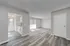 Modern open-plan living area with sleek wood flooring, abundant natural light, and a cozy kitchen space featuring white cabinetry in an inviting apartment layout.