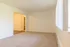 Bright and spacious living room with large window, fresh carpet, and an open doorway leading to additional space.