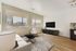 Bright and modern living room with floor-to-ceiling windows, stylish furniture, and a sleek entertainment setup, offering stunning cityscape views.