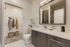 Modern bathroom featuring sleek wood cabinetry, a large mirror, and a convenient walk-in closet with cozy decor.