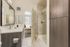 Modern bathroom with sleek vanity, glass-enclosed shower, and a glimpse into a sunlit bedroom.