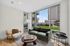Modern living room with large windows offering stunning views, featuring a green sofa, cozy chair, and elegant coffee table.