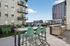 Modern outdoor patio space featuring chic bar stools, a sleek countertop, and lush green seating area in an urban apartment setting, perfect for relaxation and city views.