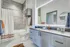 Elegant bathroom featuring a modern vanity with sleek cabinetry, spacious mirror with lighting, and a stylish shower-tub combo for a luxurious feel.