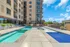 Luxurious apartment complex with a stylish outdoor pool area, complete with sun loungers and stunning city views, perfect for relaxing under clear blue skies.