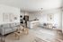 Chic open-concept living space with modern gray sofa, sleek kitchen, and stylish dining area, enhanced by elegant art on white walls.