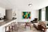 Modern apartment living area featuring a cozy lounge chair, vibrant abstract artwork, and a sleek kitchen with bar seating.