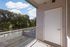 Charming apartment balcony with sleek glass railing overlooking lush green trees and a clear blue sky.