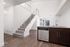 Contemporary apartment interior showcasing a sleek kitchen with granite countertops, modern cabinetry, and a stylish staircase leading to an upper floor.