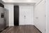Modern apartment entryway showcasing sleek stainless steel refrigerator, stylish dark cabinetry, and elegant wood flooring.