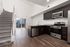 Inviting modern kitchen with sleek dark cabinets, stainless steel appliances, and a granite countertop, adjacent to an elegant staircase and sunlit balcony.