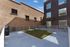 Modern urban rooftop terrace featuring a neatly manicured lawn area, sleek metal railings, and stylish seating against a backdrop of textured brick and glass facade.