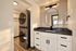 Modern apartment laundry area featuring stacked washer and dryer, elegant vanity with large round mirror, and sleek tile backsplash.