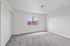 Bright and spacious empty room with plush carpet and large window offering scenic views of neighboring rooftops.