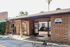Charming office entrance with rustic brick design and welcoming open doors, surrounded by lush greenery and inviting natural light.