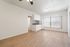 Bright apartment featuring a modern kitchen with sleek cabinetry, open living area with wood flooring, and large windows with vertical blinds.
