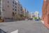 Spacious urban courtyard with modern apartment buildings and ample parking, bathed in bright sunlight.