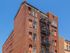 Charming historic brick apartment building with classic fire escape, showcasing vintage urban architecture under a clear blue sky.