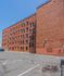 Charming urban apartment building with classic red brick exterior and convenient parking spaces under a clear blue sky.