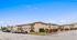 Charming corner apartment complex with well-maintained landscaping and ample parking, set against a clear blue sky.