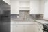 Modern kitchen with sleek black refrigerator, elegant tiled backsplash, and ample white cabinetry.