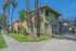 Charming suburban apartment building with lush landscaping and vibrant greenery, highlighted by tall palm trees and a secure gated entrance.