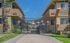 Inviting entryway to a cozy apartment complex, featuring charming stucco buildings and lush greenery under a clear blue sky.