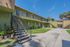 Sunny courtyard view of a vibrant apartment complex with charming green facades and open staircases, surrounded by lush greenery.