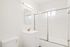 Bright, modern bathroom with sleek white vanity, elegant mirror, and spacious shower with sliding glass doors.