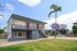 Charming two-story apartment building with modern design, surrounded by lush greenery and vibrant purple trees, set in a serene neighborhood.