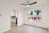 Bright apartment interior with a sleek ceiling fan, large window view of palm trees, and modern kitchen entrance.