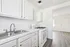 Bright kitchen with modern white cabinetry, dual stainless steel sink, and an efficient gas stove, leading into a sunlit open living space with elegant flooring.