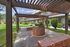 Charming courtyard view featuring a rustic pergola and brick BBQ area, surrounded by lush greenery and modern apartment buildings.