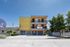 Charming apartment building with modern balconies, vibrant yellow facade, and lush greenery, inviting you to schedule a visit.