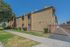 Charming two-story apartment complex with a gated entrance, surrounded by manicured greenery and a clear blue sky.