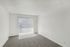Bright and spacious apartment room with modern carpet flooring and abundant natural light from large sliding glass doors.