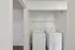Modern laundry nook featuring a sleek washer and dryer set with a convenient overhead shelf in a bright, white-walled space.