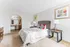 Bright and inviting bedroom featuring a plush bed with checkered and red accent pillows, a rustic bedside table with a modern lamp, and an elegant vanity space in the background.