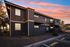 Charming two-story apartment building with wooden exterior, featuring cozy balconies against a vibrant sunset sky.