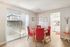 Bright dining area with vibrant red chairs and a round table, adjacent to a modern kitchen, overlooking a sunlit patio.