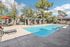 Tranquil outdoor pool area featuring sun loungers, shaded pergolas, and vibrant landscaping under a clear blue sky.
