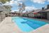Inviting apartment complex pool area with crystal-clear water, surrounded by sun loungers and shaded by red umbrellas, perfect for relaxation and leisure.