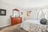 Inviting bedroom with plush floral bedding, elegant wooden dresser with mirror, and bright natural light streaming through the window.